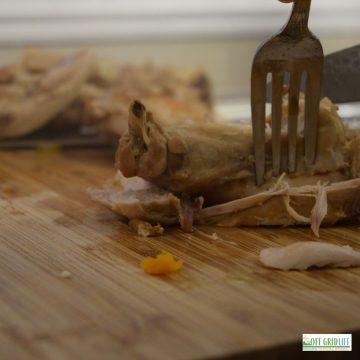 a fork and knife cutting meat off of a bone on a wooden cutting board