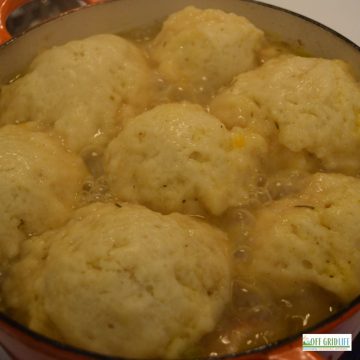 puffy dough dumplings rising on top of a stew in a dutch oven