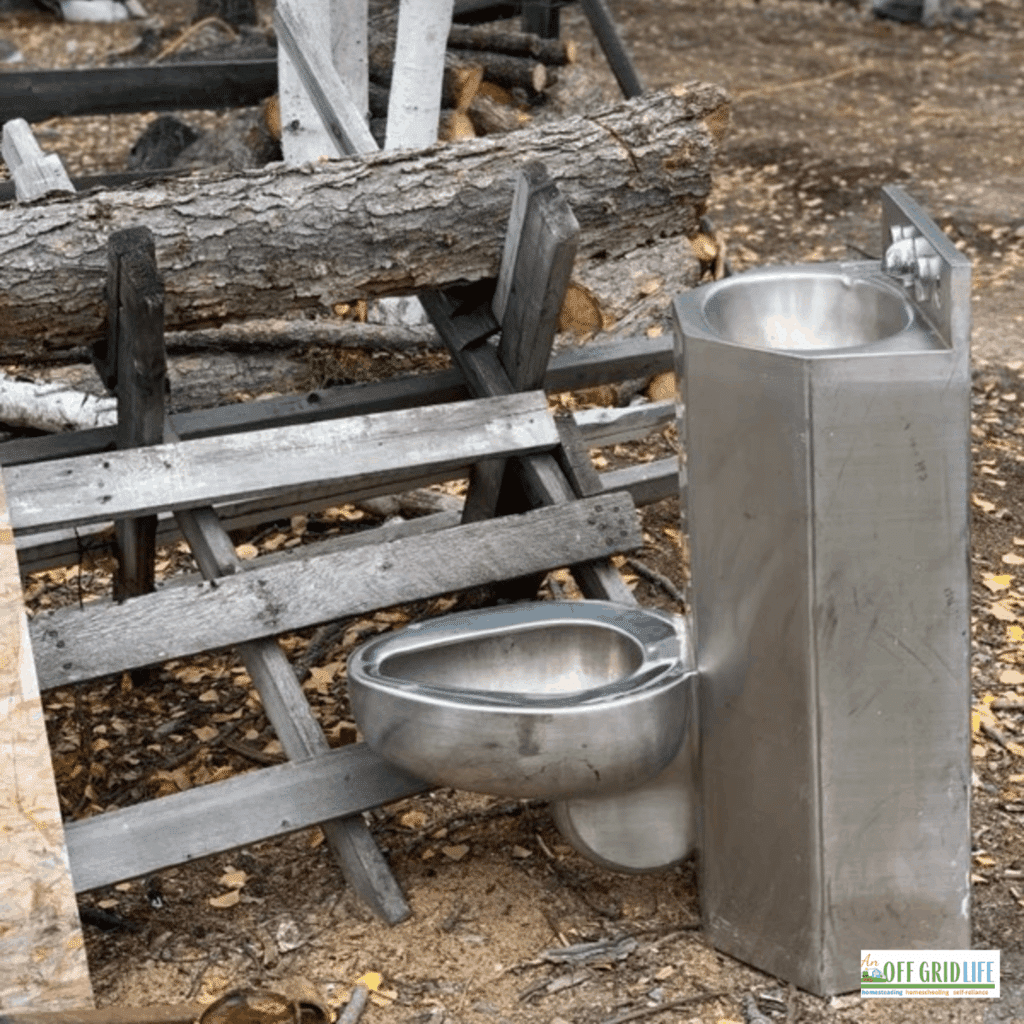 A stainless steel toilet and sink next to a wooden fence outdoors.