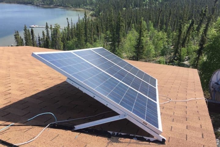 A solar panel installed on a roof with a lake and forest in the background.