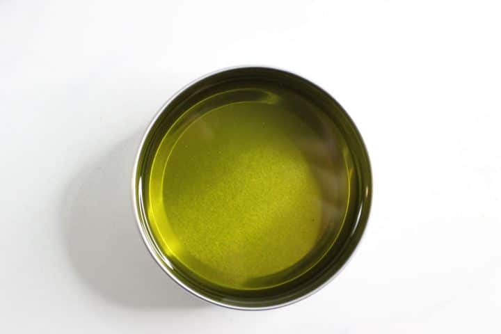 A metal bowl filled with olive oil on a white background.