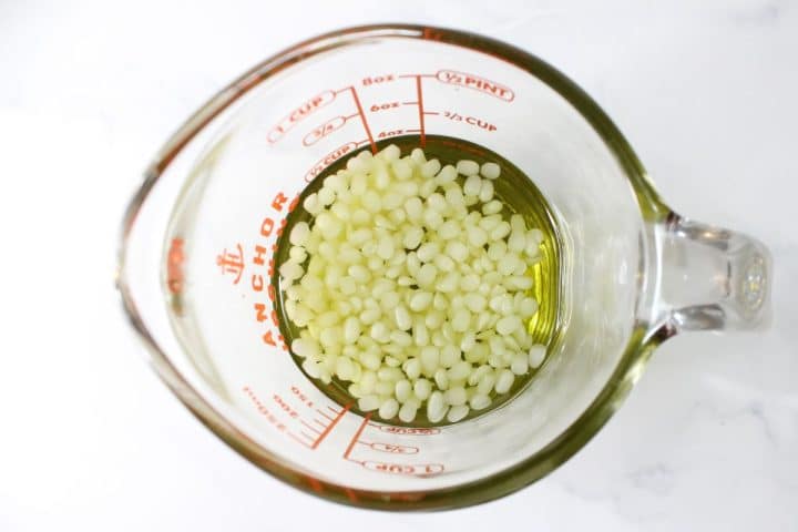 A glass measuring cup containing small white beads and a yellow liquid, with measurement markings on the cup, placed on a white surface.