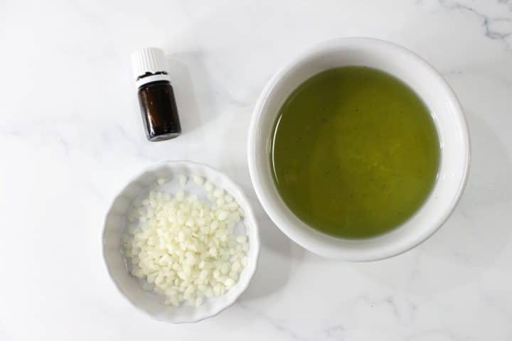 A small bottle, a bowl of green liquid, and a bowl of white pellets on a marble surface.
