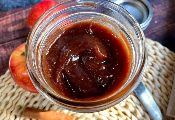 A jar of homemade crockpot apple butter with apples and cinnamon.
