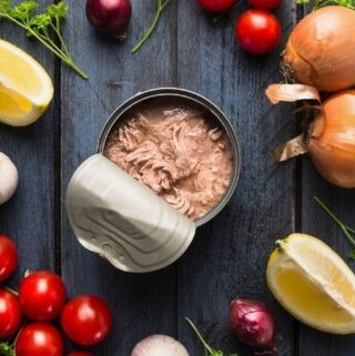 A picture of a can of fish surrounded by fresh vegetables