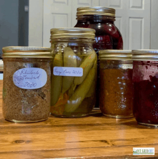5 mason jars with pickled vegetables and preserves on a wooden counter