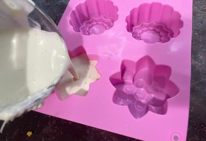 A pink flower shaped mold is being filled with homemade shampoo.