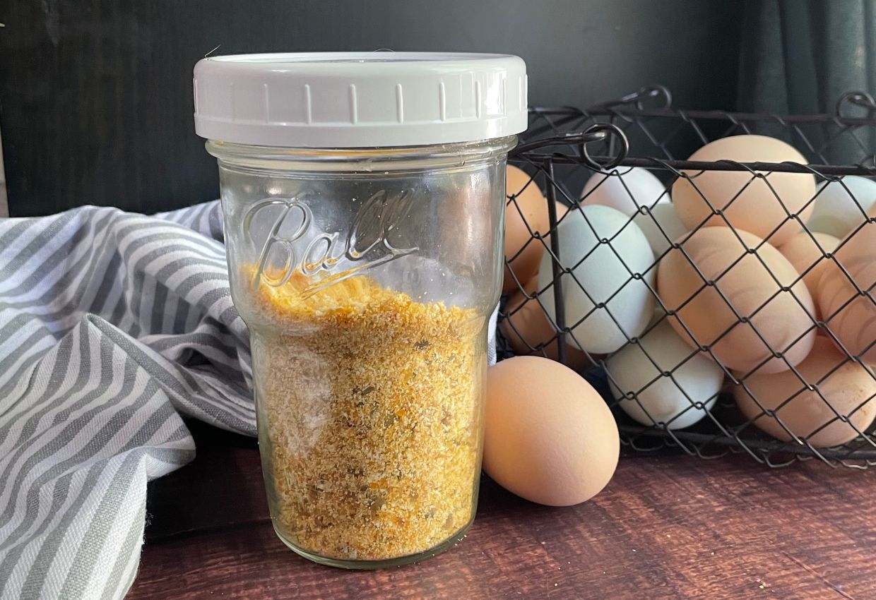 Dehydrated eggs in jar with basket of fresh eggs behind.