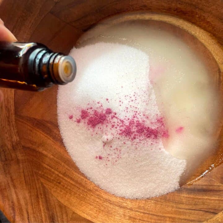 A person pouring essential oil into a wooden bowl.