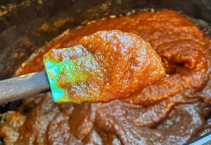 A spoon is being used to stir pumpkin butter in a slow cooker.