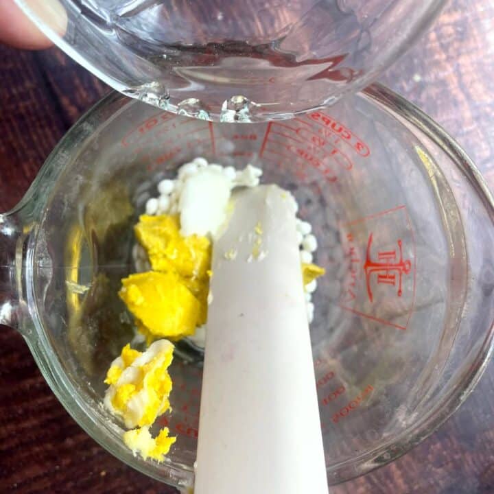 A person pouring eggs into a glass measuring cup.