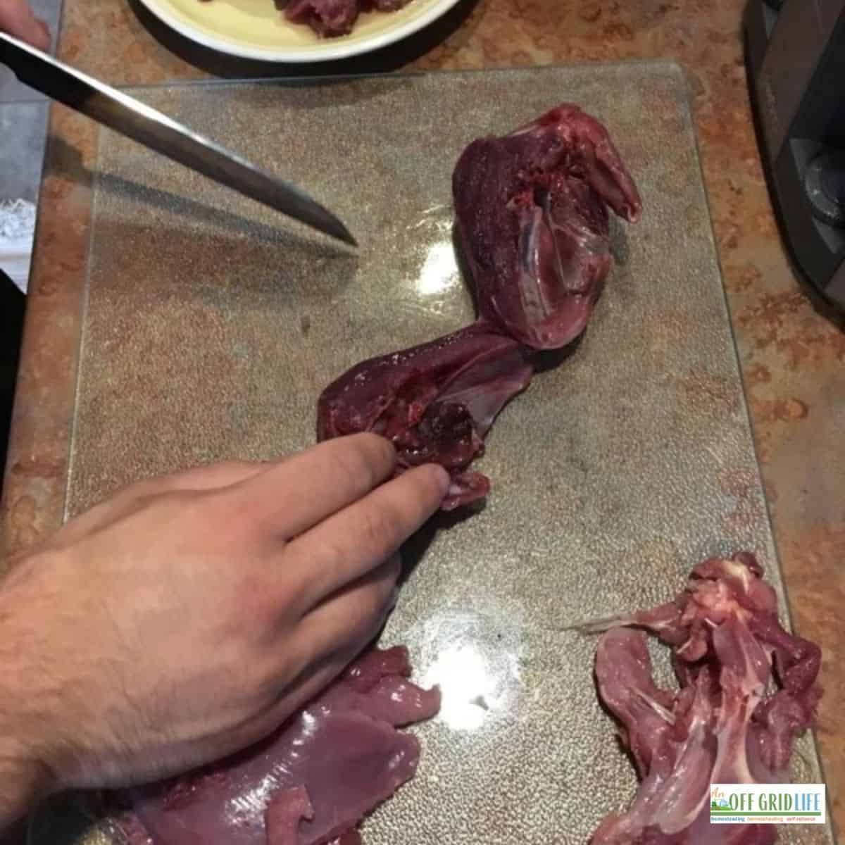 a mans hands with a chef's knife cutting up ptarmigan breasts on a glass cutting board