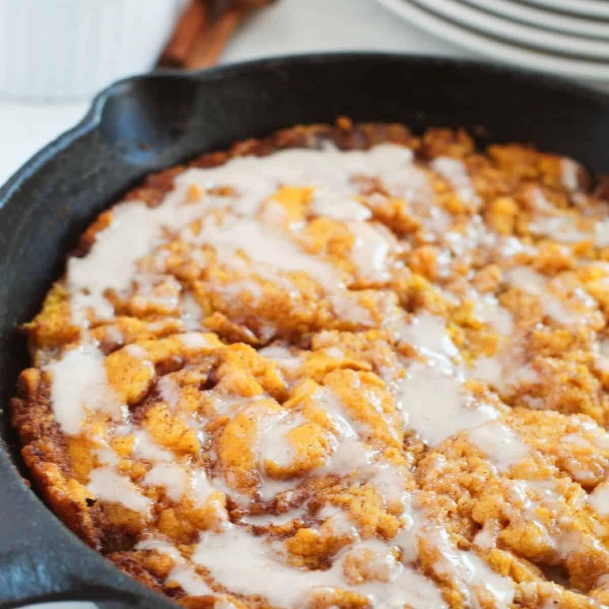 Pumpkin Cinnamon Roll Skillet Cake with icing in a cast iron skillet on a wooden table top