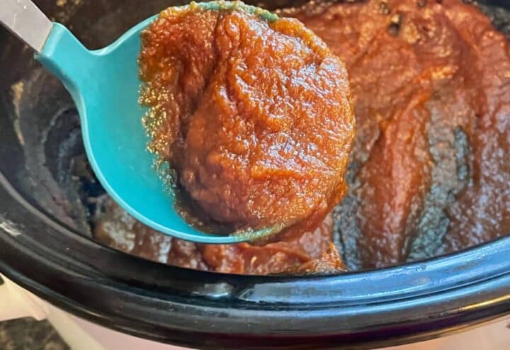 A spoon is being used to stir a sauce in a crock pot.