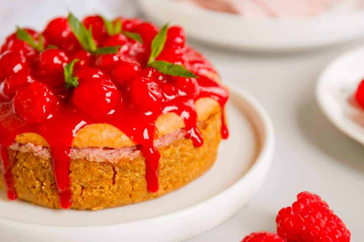 A raspberry-topped cheesecake with raspberry sauce on a white plate.