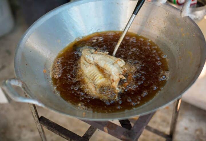 A person is frying a piece of fish in a pan.