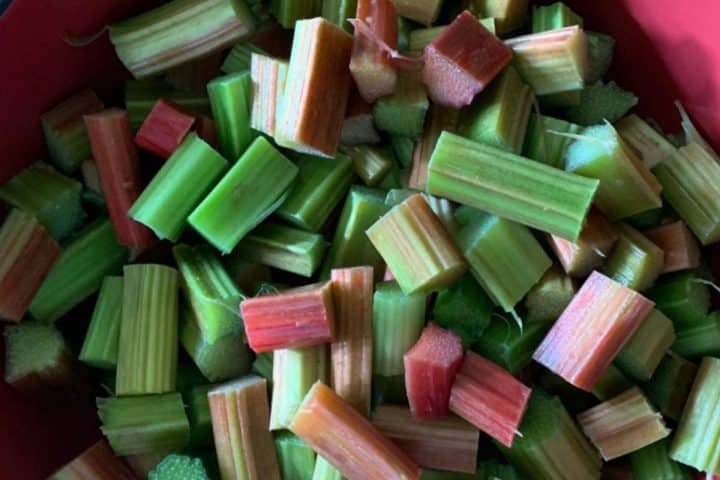 Chopped green and red rhubarb stalks in a red bowl.
