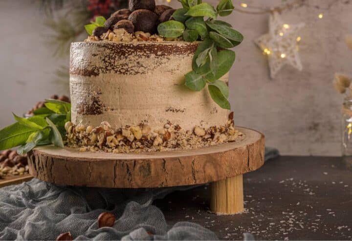 A chocolate cake with nuts and greenery on a wooden stand.