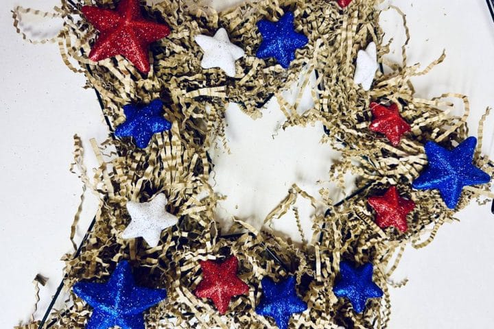 A decorative wreath adorned with red, white, and blue glittery stars and crinkled paper filler on a white background.