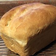 A loaf of freshly baked bread rests on a cooling rack next to a butter knife on a brown countertop.
