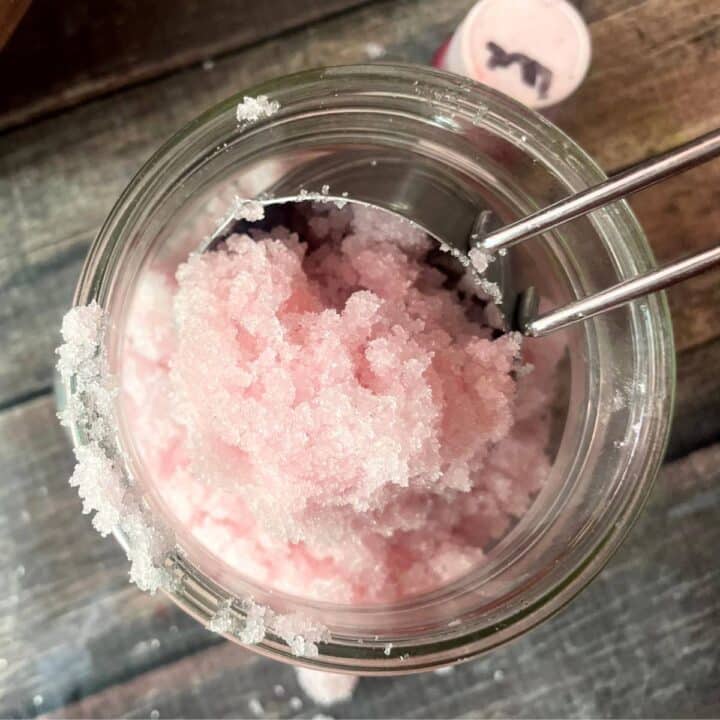 Pink peppermint sugar scrub in a jar with a spoon.