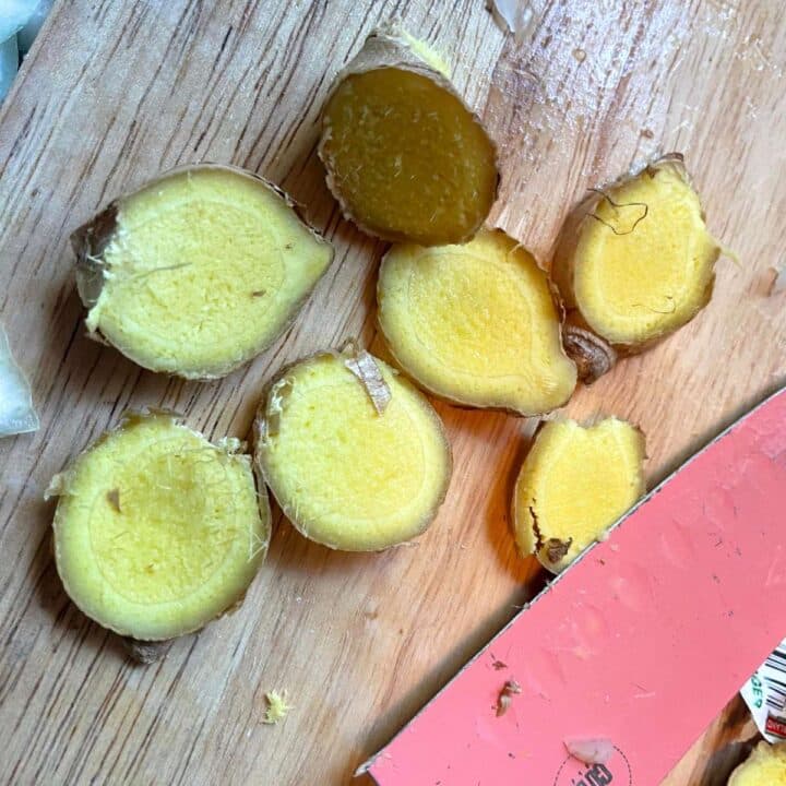 Sliced ginger on a cutting board with a knife.