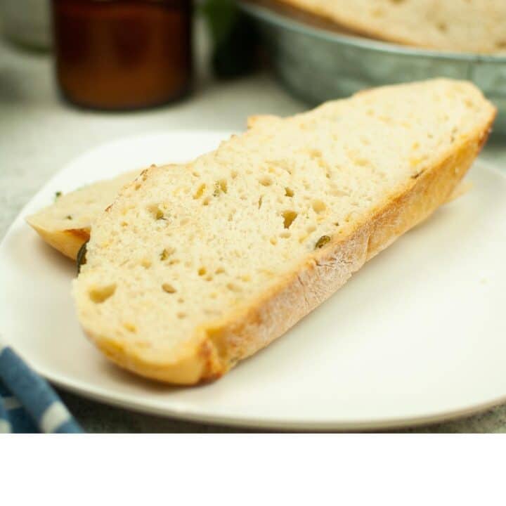 A slice of cheddar jalapeno bread on a plate next to a bottle of olive oil.