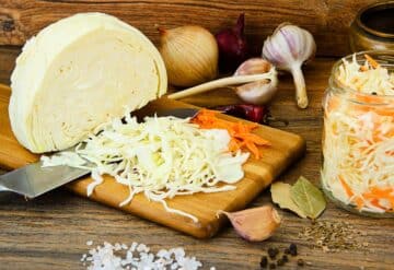 A cutting board with carrots, onions, and garlic on it.