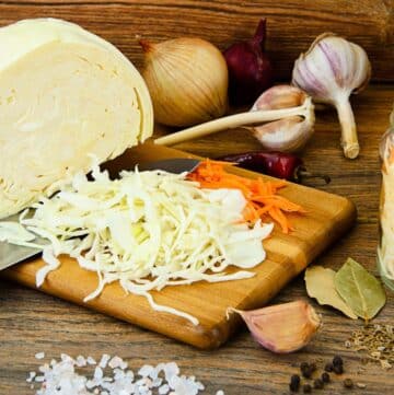 A cutting board with carrots, onions, and garlic on it.