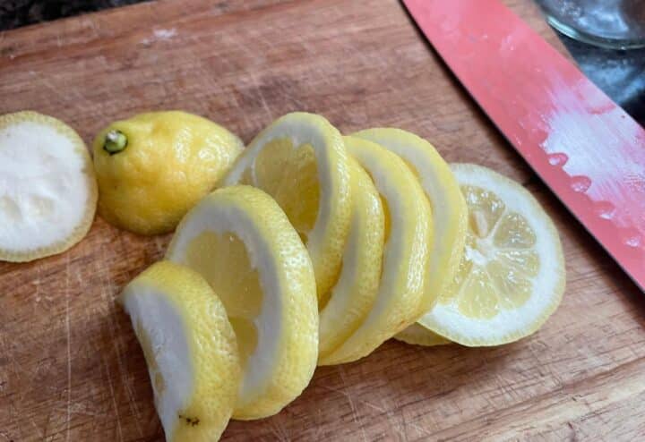 Sliced lemons on a cutting board next to a knife.