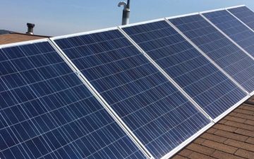 a five panel solar array on a brown shingle roof with a blue sky background