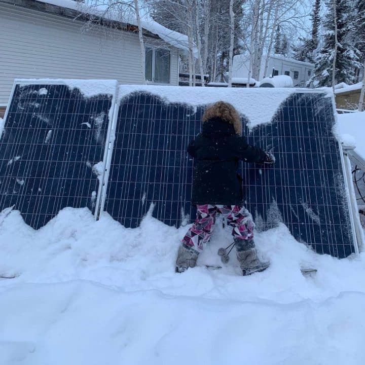 A little girl standing next to a solar panel covered in snow.