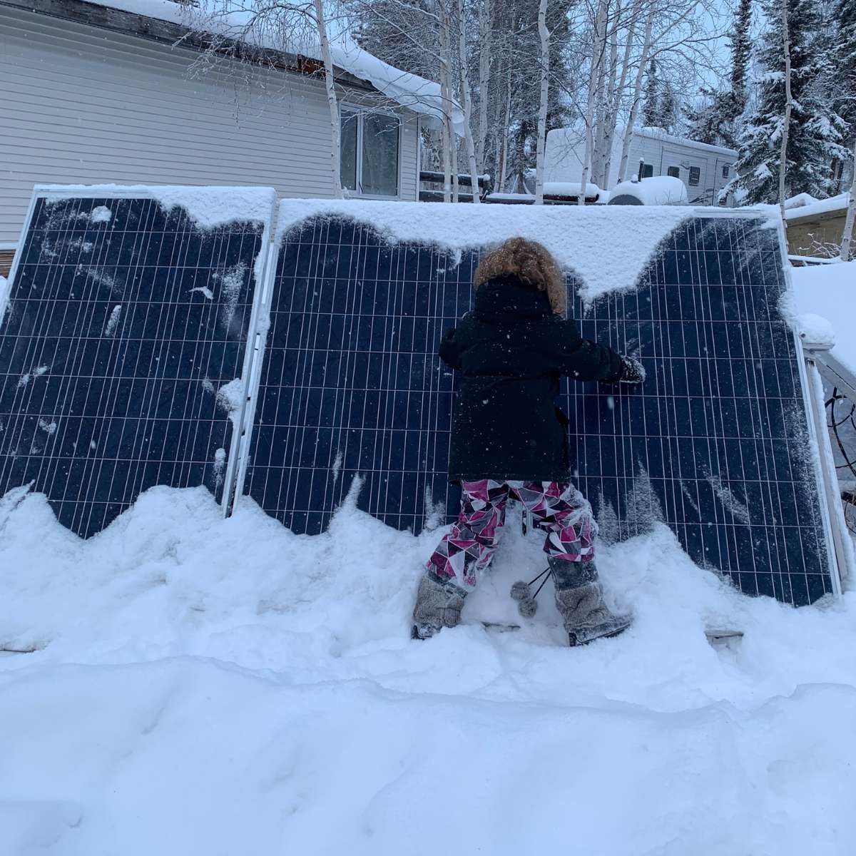 A little girl standing next to a snow-covered solar panel, showcasing the potential to survive off the grid with renewable energy.