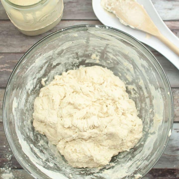 A bowl of sourdough and a jar of sourdough starter on a wooden table.