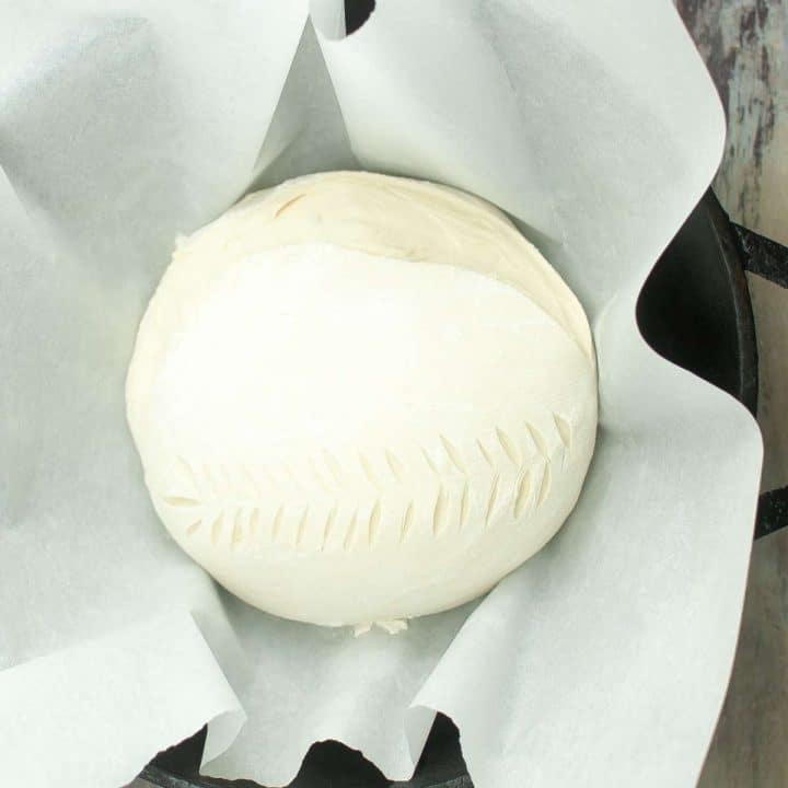 A ball of sourdough in a dutch oven on top of a wooden table.