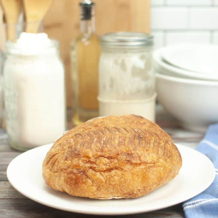 A loaf of dutch oven sourdough bread on a plate next to a bowl of flour.