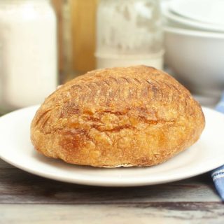 A loaf of dutch oven sourdough bread sitting on a white plate.