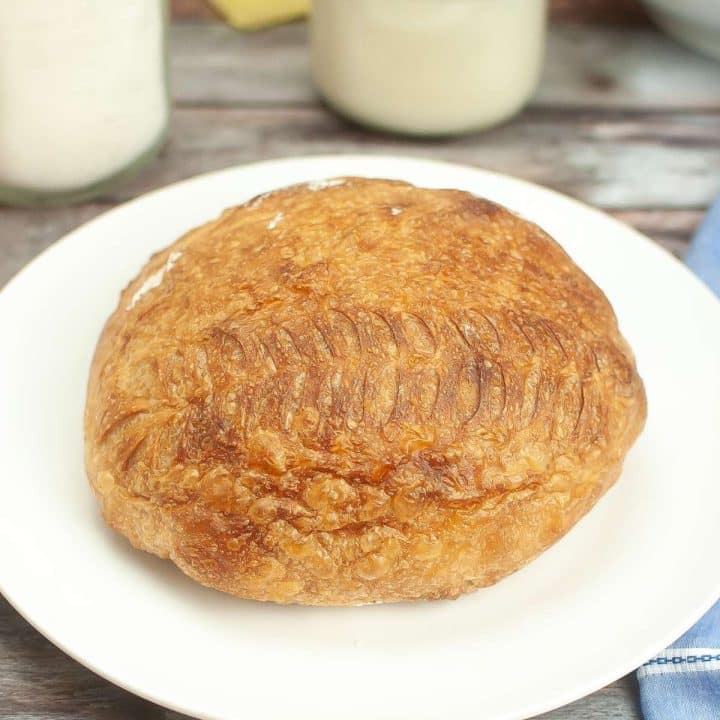 A loaf of dutch oven sourdough bread on a plate next to a jar of milk.