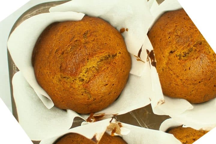 Three freshly baked muffins in white parchment paper, placed in a baking tray.