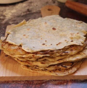 Stack of sourdough starter discard tortillas on a wooden cutting board.