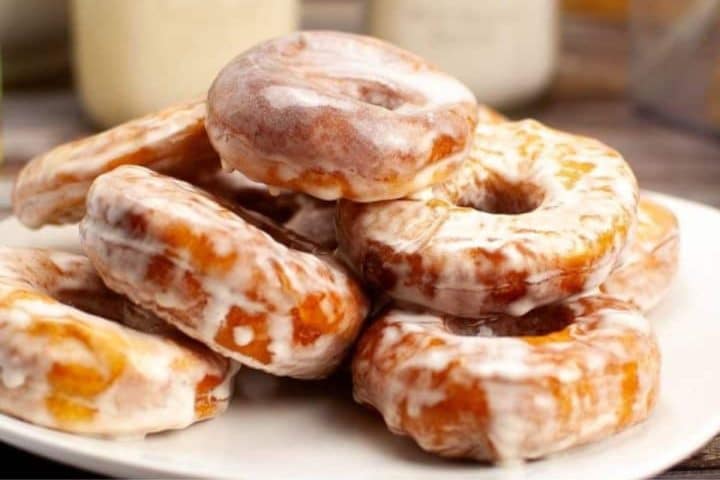 A plate stacked with glazed donuts, showing smooth, shiny icing, placed on a table.