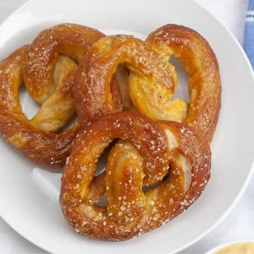 Three sourdough pretzels served on a white plate next to a blue napkin.