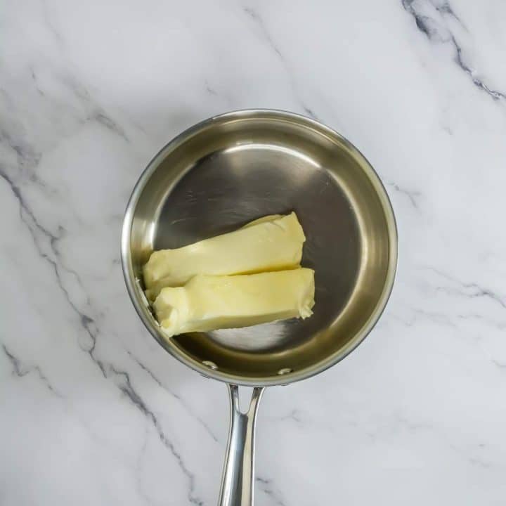 Two pieces of butter in a pan on a marble countertop.