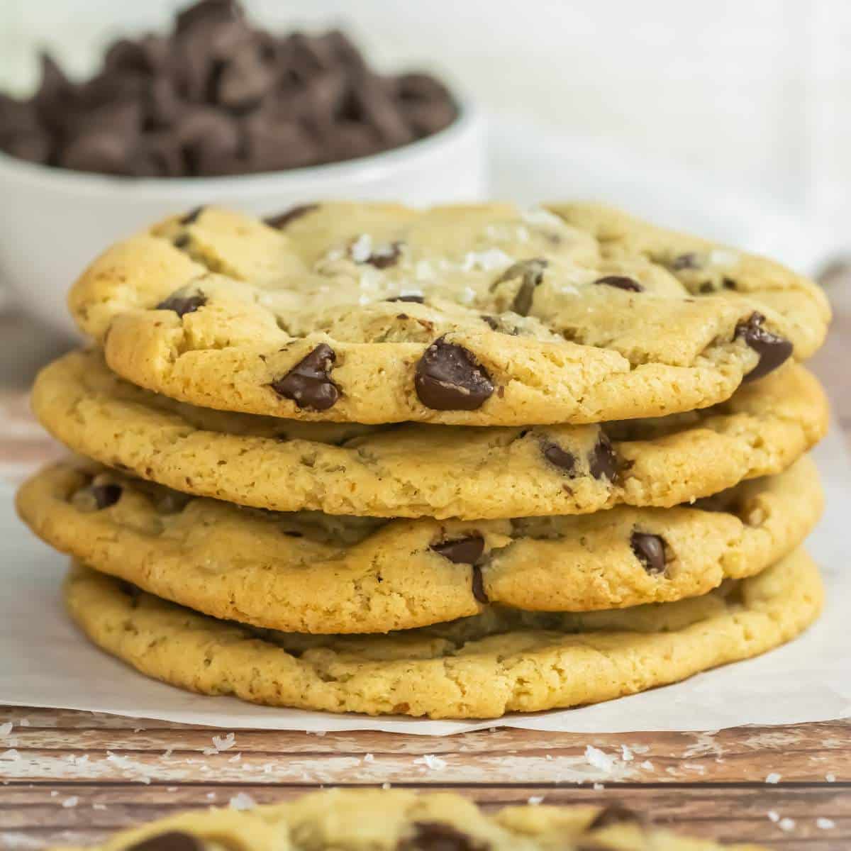 A stack of sourdough chocolate chip cookies next to a bowl of chocolate chips.