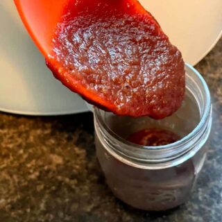A spoon is being used to pour apple butter into a jar.
