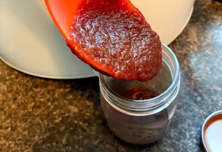A spoon is being used to pour apple butter into a jar.