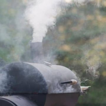 A black charcoal smoker with smoke coming out of the top dampener