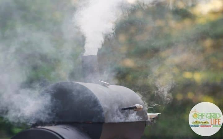 A black charcoal smoker with smoke coming out of the top dampener