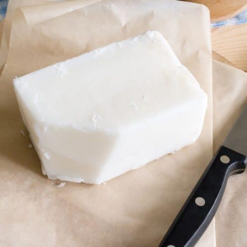 A block of tallow rests on parchment paper beside a black-handled knife, reminiscent of traditional uses for tallow in cooking and crafts.