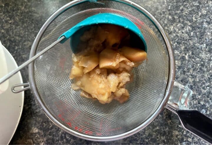 Apples in a strainer with a spoon.